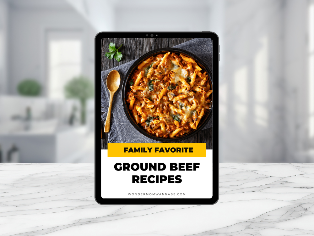 A tablet on a marble counter in a bright kitchen displays the Wondermom Wannabe "Family Favorite Ground Beef Recipes Digital Cookbook," featuring easy ground beef recipes.