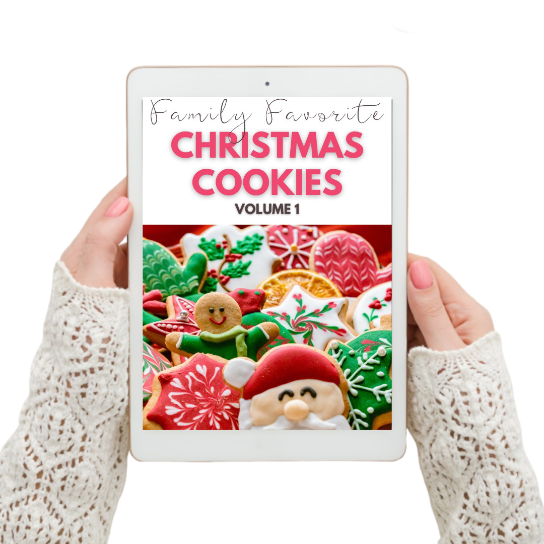 A woman holding an iPad displaying a digital cookbook titled "Family's Favorite Christmas Cookies Digital Cookbook Volume 1" by Wondermom Wannabe.