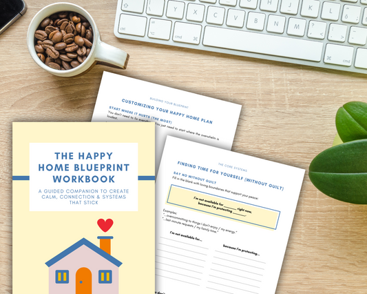 The Happy Home Blueprint Workbook: Printable Tools to Simplify Your Home Life by Wondermom Shop lies open on a desk with a keyboard, coffee, and a green plant—the perfect companion for organizing your space.