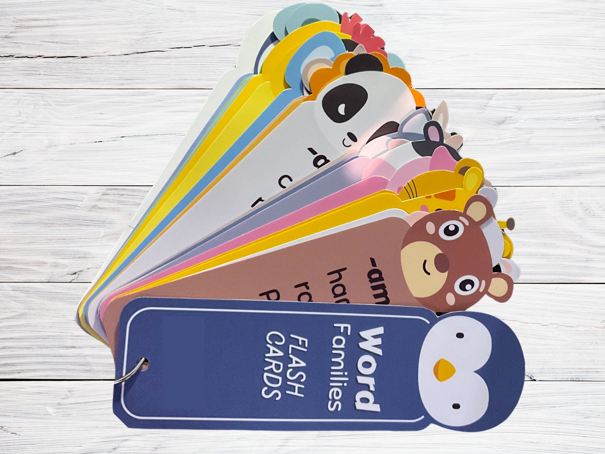 Fan of colorful, animated Wondermom Shop Printable CVC Word Family Flash Cards spread out on a wooden surface.