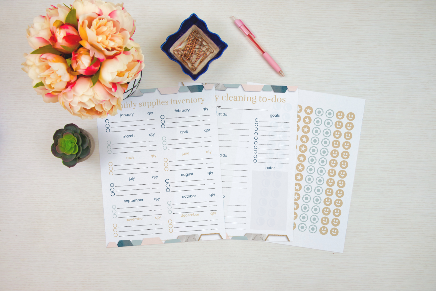 Overhead view of planners with floral and succulent decor, featuring Wondermom Shop's Cleaning Binder: Your Go-To Guide for a Spotless Home, supplies inventory, chore charts, and a sheet of stickers on a light surface.