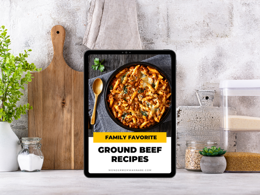 On a kitchen counter, the Wondermom Wannabe Family Favorite Ground Beef Recipes Digital Cookbook displays a pasta dish cover, surrounded by cooking essentials—perfect for discovering easy, budget-friendly ground beef meals.