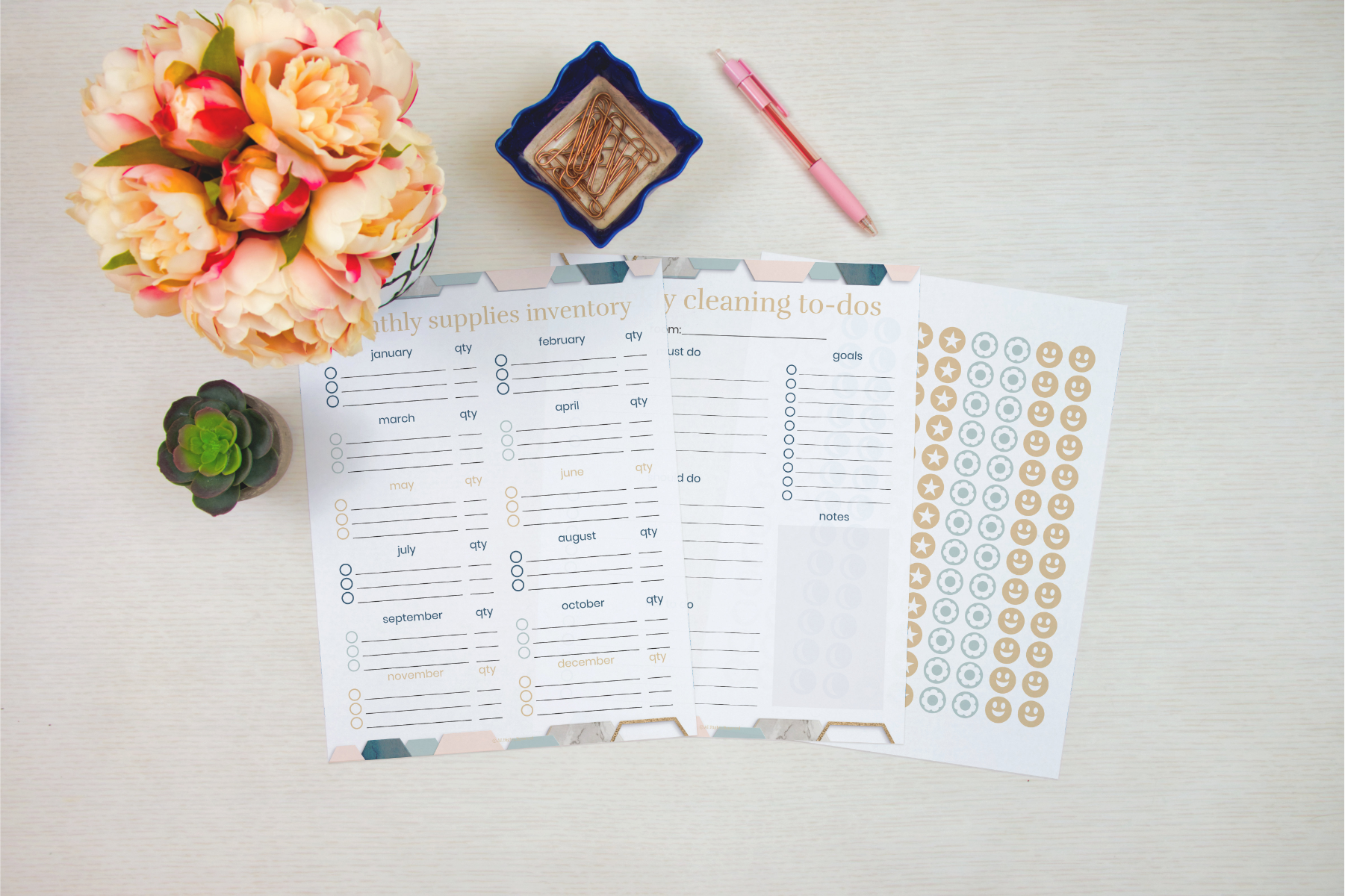 Overhead view of planners with floral and succulent decor, featuring Wondermom Shop's Cleaning Binder: Your Go-To Guide for a Spotless Home, supplies inventory, chore charts, and a sheet of stickers on a light surface.