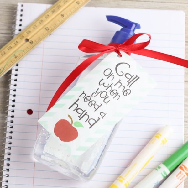A bottle of Hand Sanitizer Teacher Gift by VIP Vault next to a notebook and pencils.