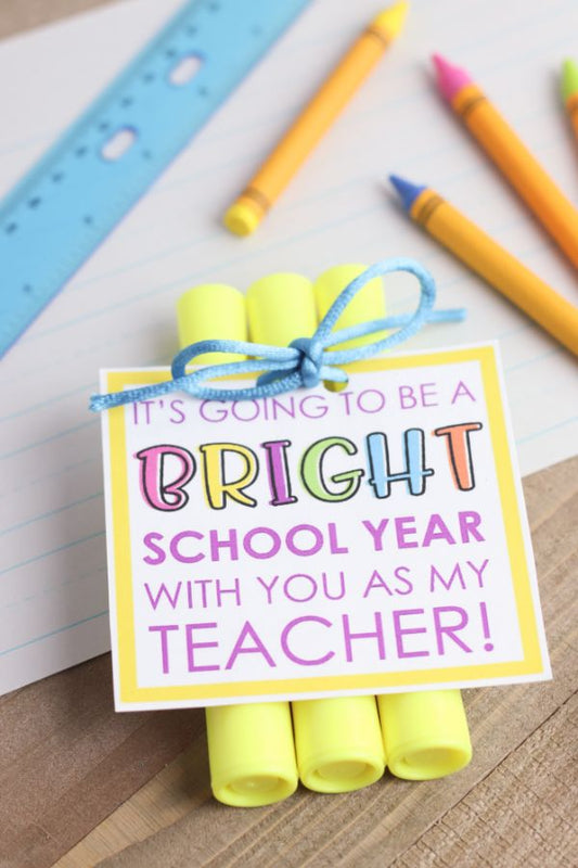 VIP Vault's Highlighter Teacher Gift features three yellow highlighters tied with blue string and a printable tag: "It's going to be a BRIGHT school year with you as my teacher!" Great digital gift for any educator. Crayons, ruler, and paper included in the background.