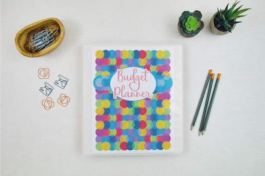 A colorful Budget Planner from Wondermom Shop with pens and pencils next to it.